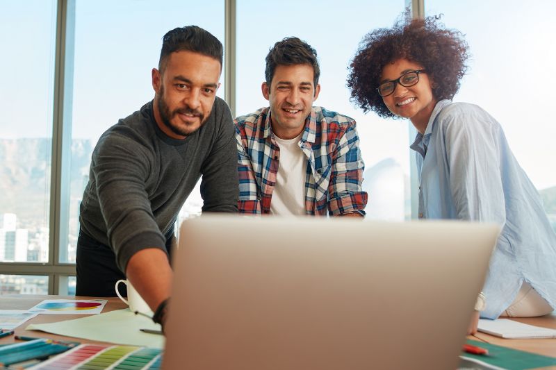 three people standing over a laptop smiling